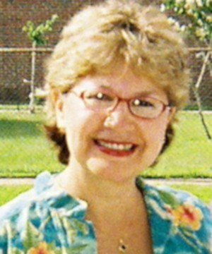 Carmen Abber is wearing blondish short hair cut, glasses, green orange flower shirt, and is smiling looking front