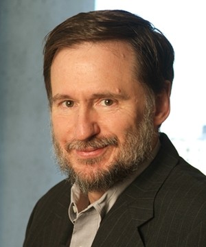 Michael Doyle wears a dark blazer and a tan collared shirt underneath while looking into the camera