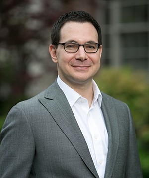 Matthew Waxman wears a grey suit, white shirt and smiles directly to the camera